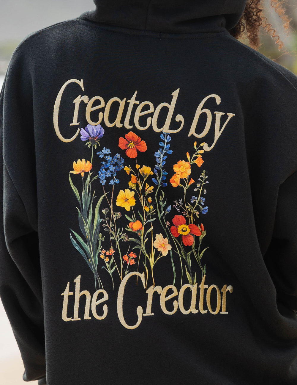 Black unisex hoodie back print close-up with 'Created by the Creator' script and flowers