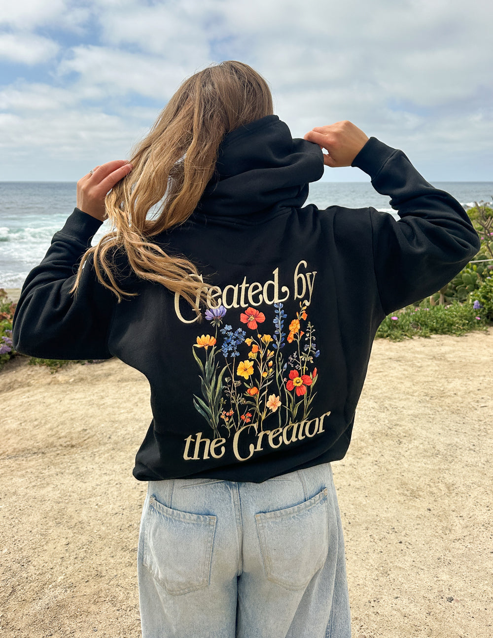 Black unisex hoodie back view with floral 'Created by the Creator' on upper back