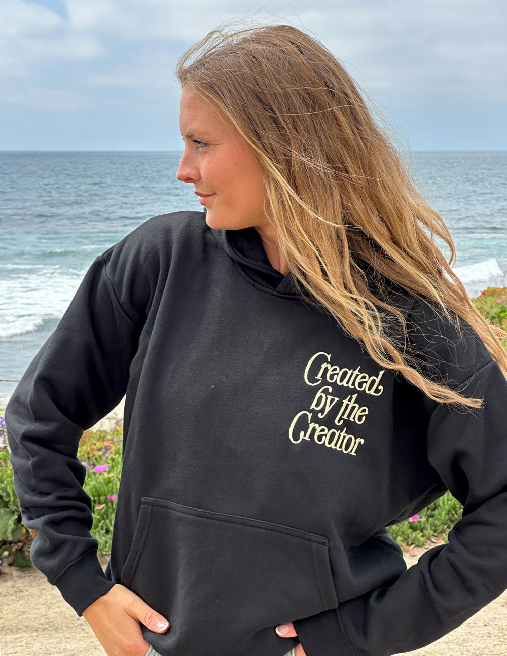 Black unisex hoodie side view with hood down and 'Created by the Creator' chest text