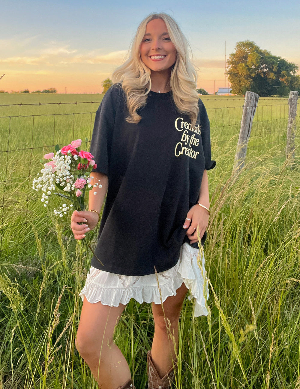 Black unisex tee with front logo text and small colorful flower graphic