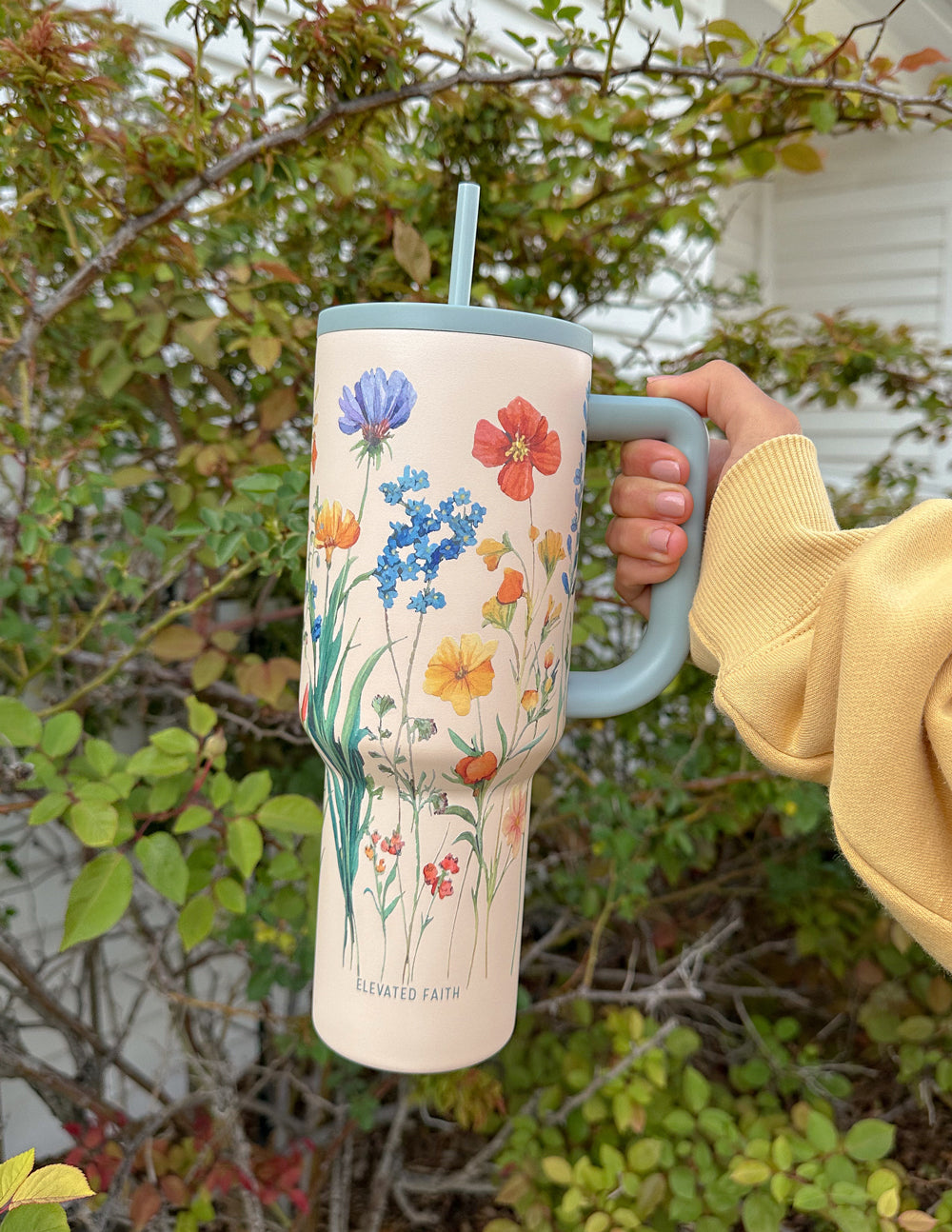 Floral 40 oz tumbler with gray handle and straw lid, held outdoors