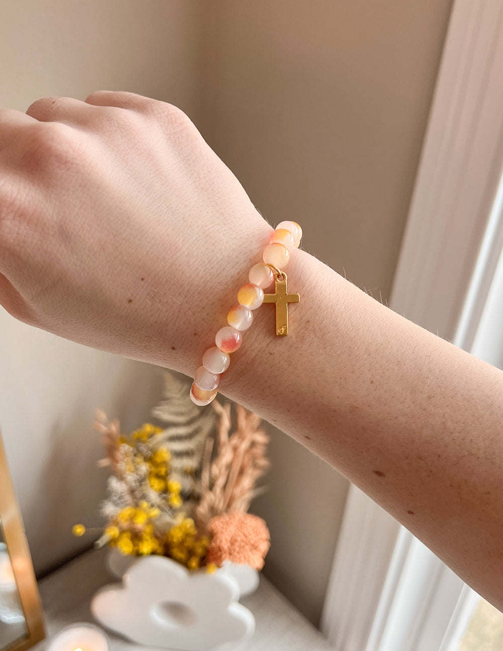 Peach and white beaded bracelet with gold cross charm on wrist