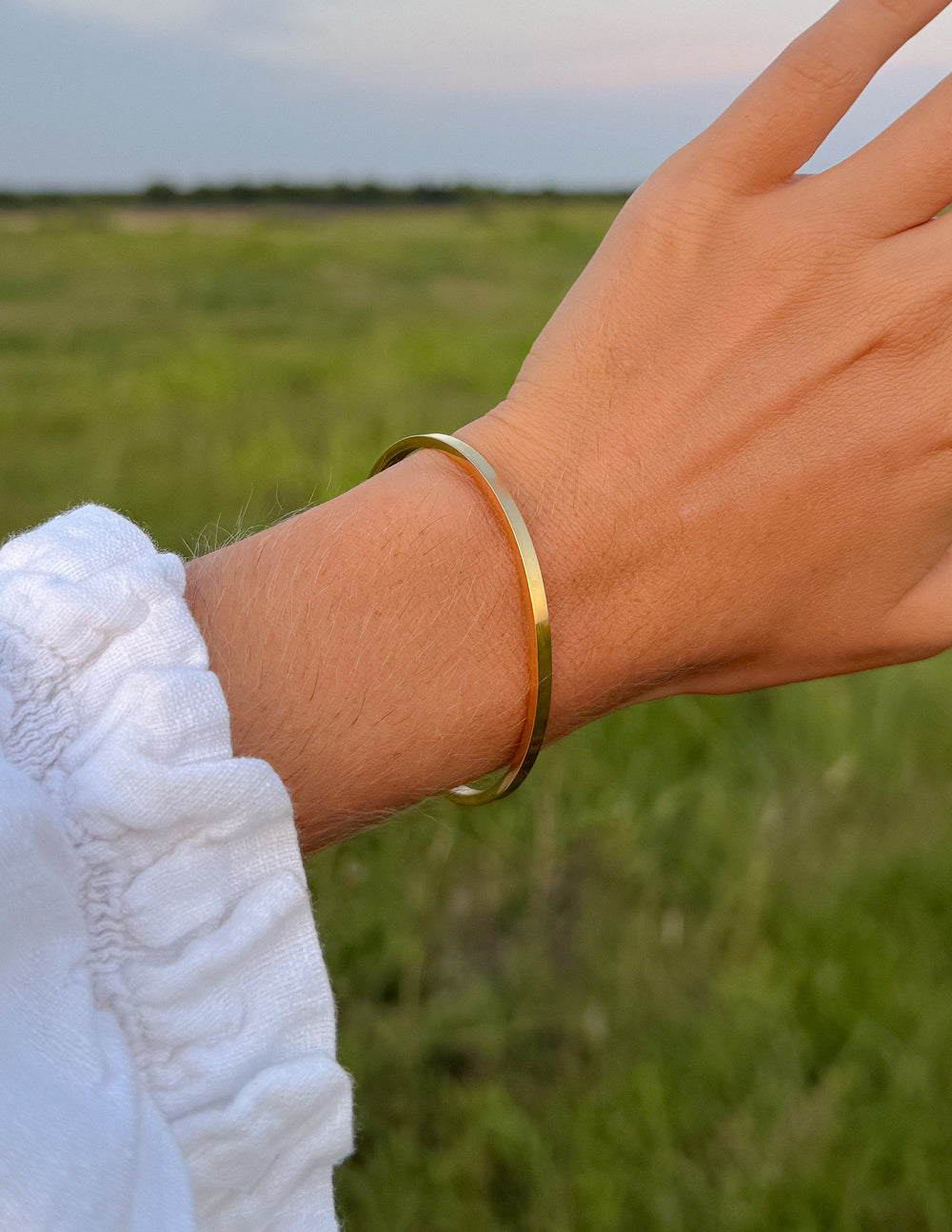 Gold cross cuff bracelet on wrist, flat bangle with cross detail