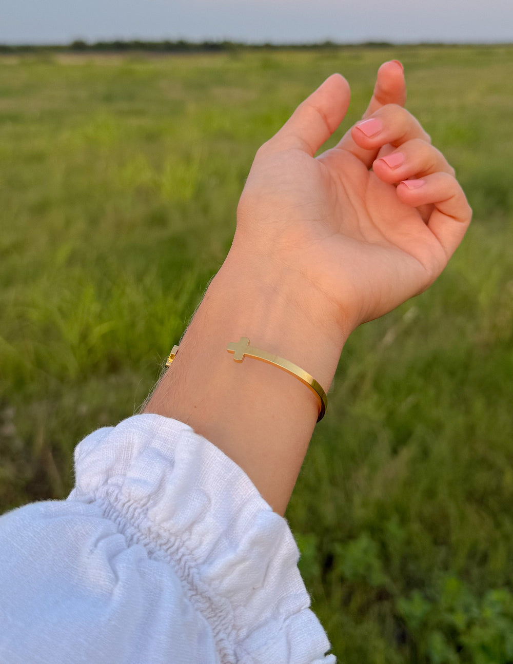 Gold cross cuff bracelet on wrist, cross charm at center