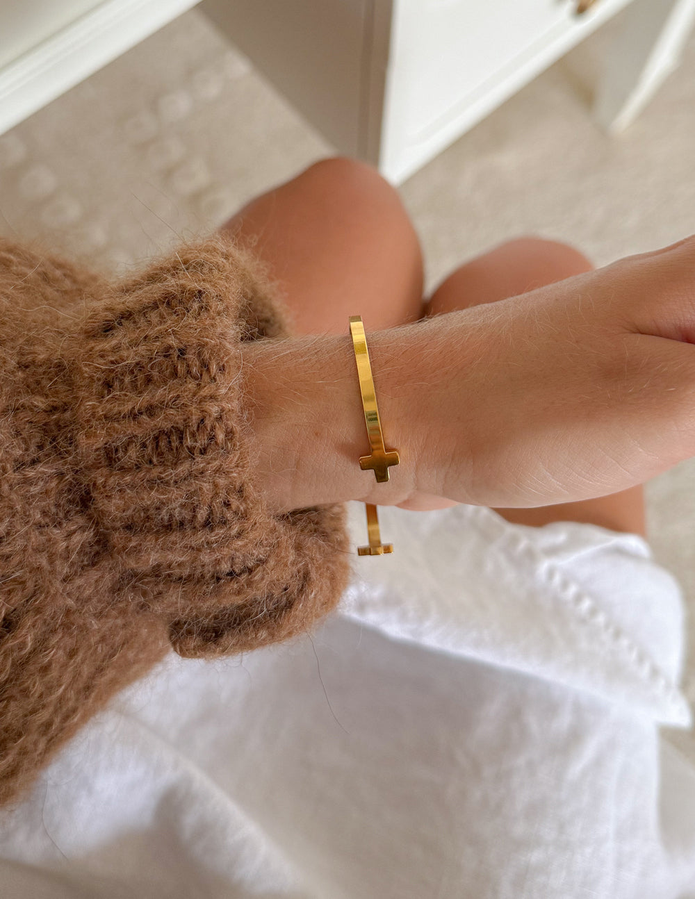 Gold cross cuff bracelet on wrist, cross ends visible