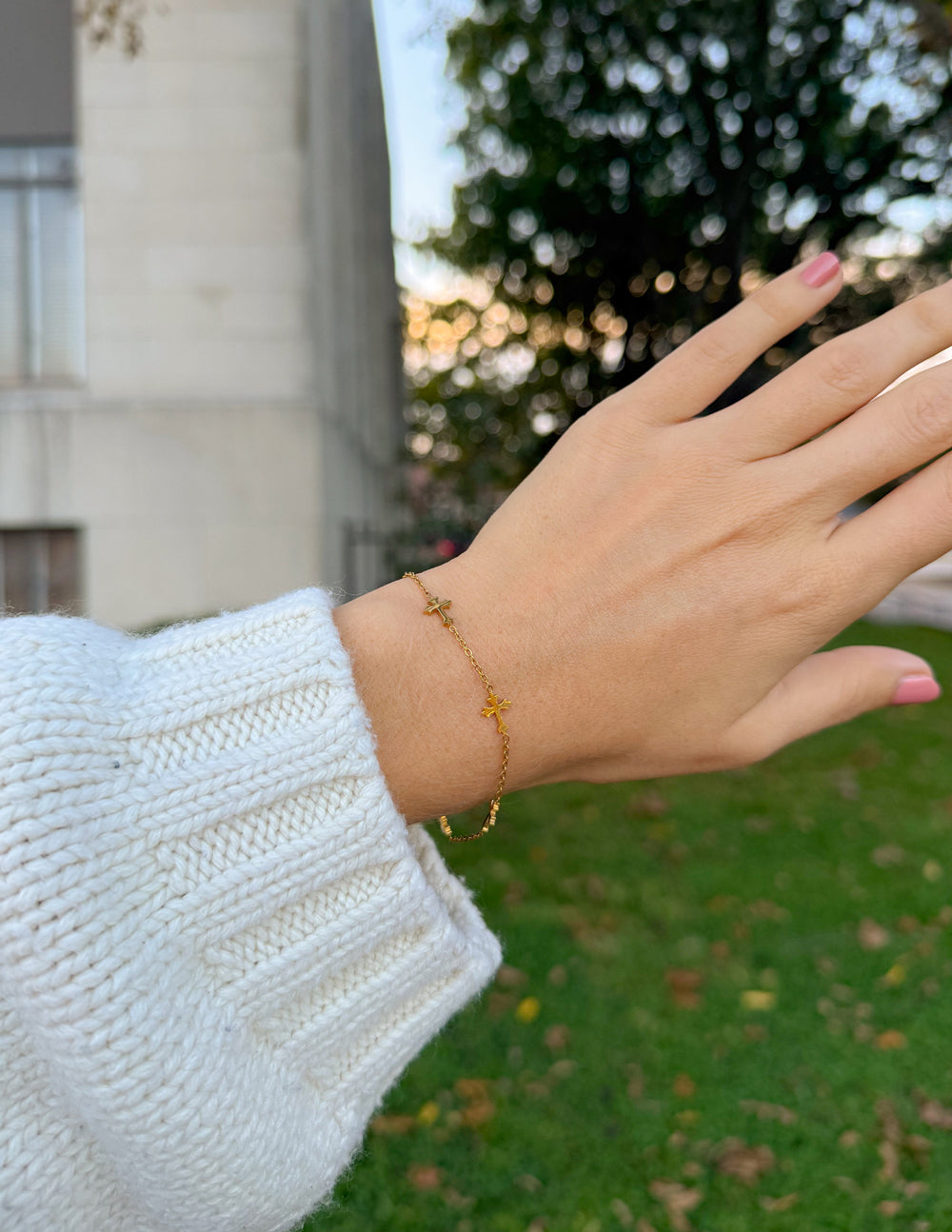 Gold cross link bracelet on wrist with small cross charms and chain links.
