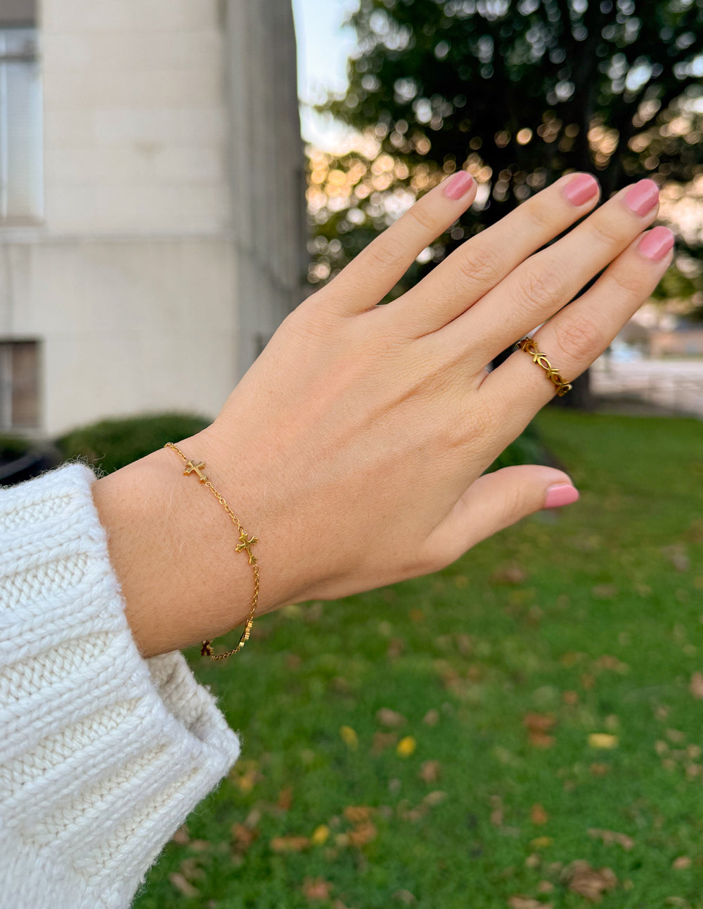 Gold cross link bracelet on wrist, cross charm drops along the chain.