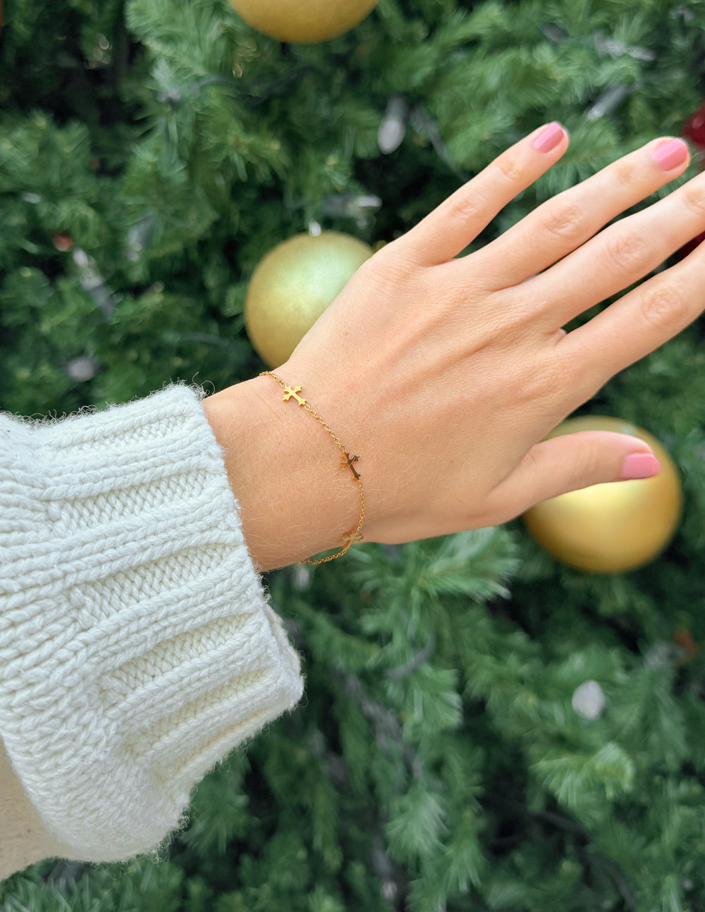 Gold cross link bracelet on wrist with dangling cross charm detail.