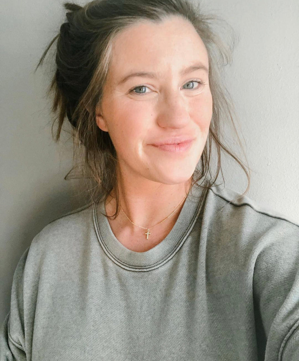 Gold cross pendant on a thin chain necklace worn with a gray top