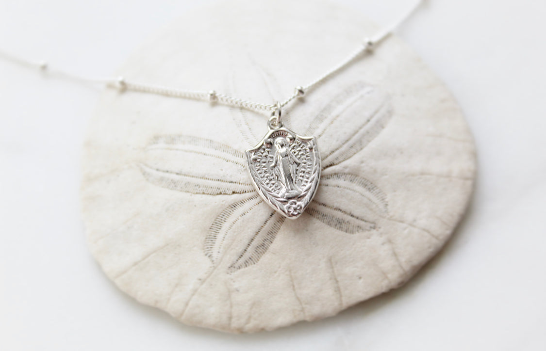 Sterling silver shield pendant necklace with Virgin Mary figure, front view on chain