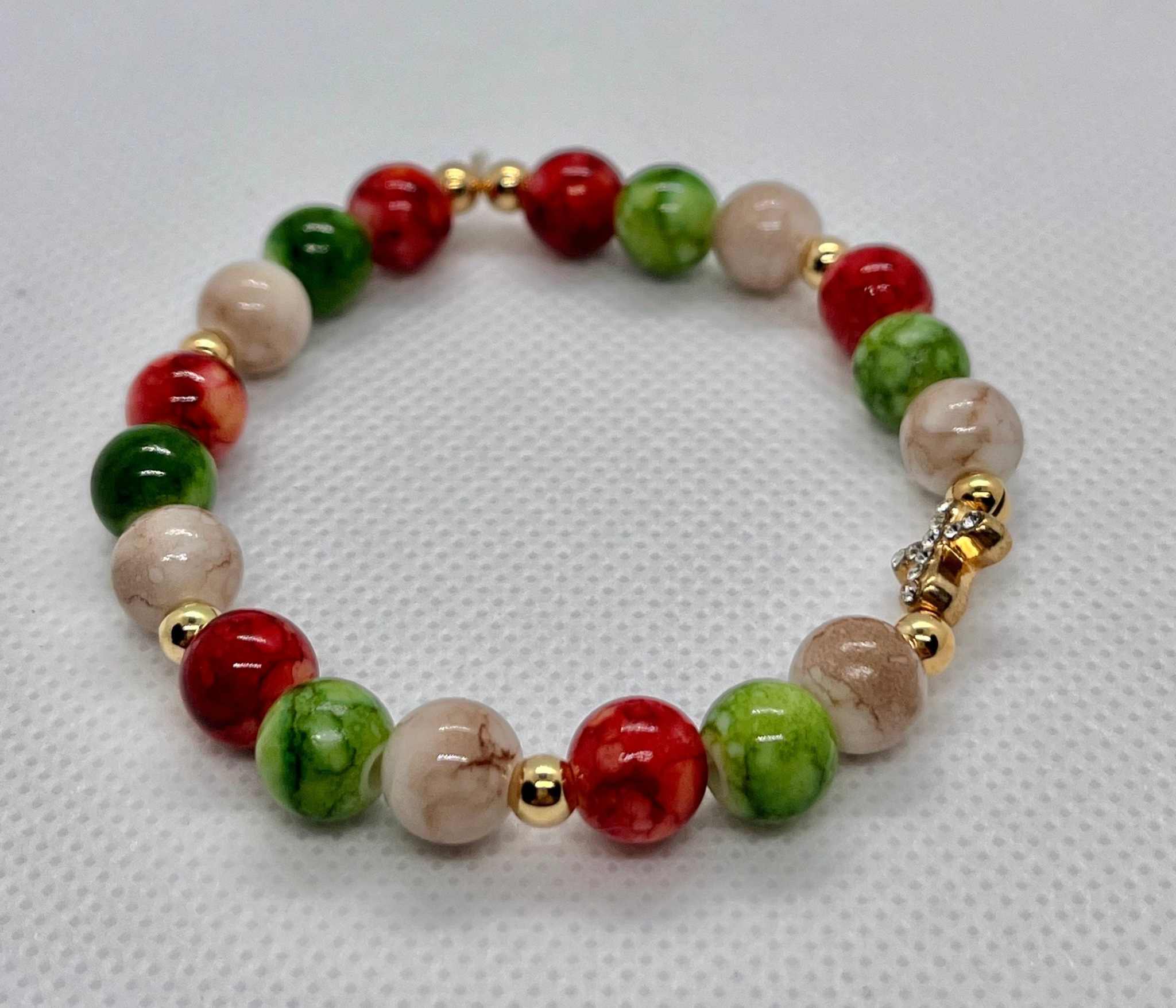 Bead bracelet with red, green, and marbled beige beads and a gold cross charm detail