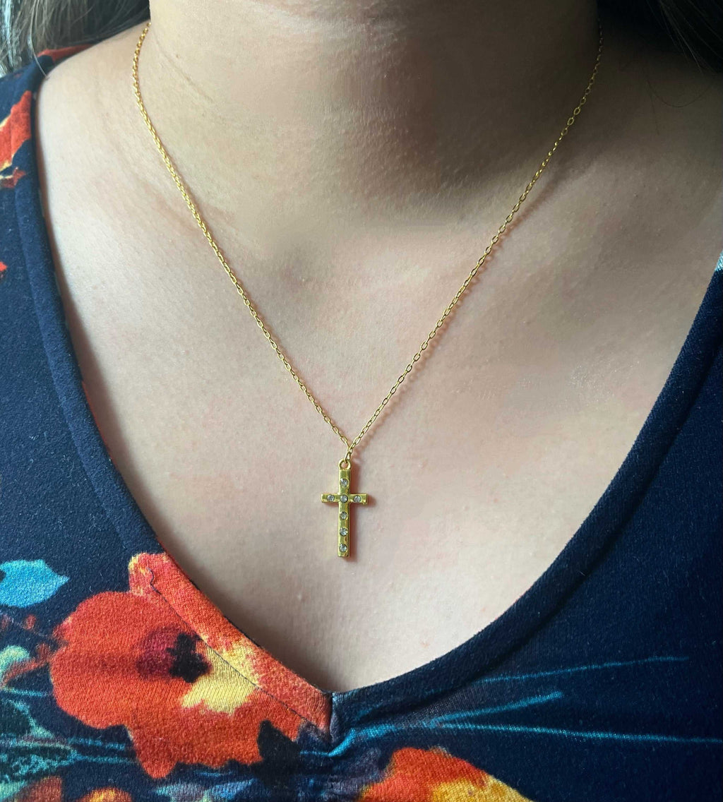 Gold cross pendant necklace close-up, cross charm with small stones on chain