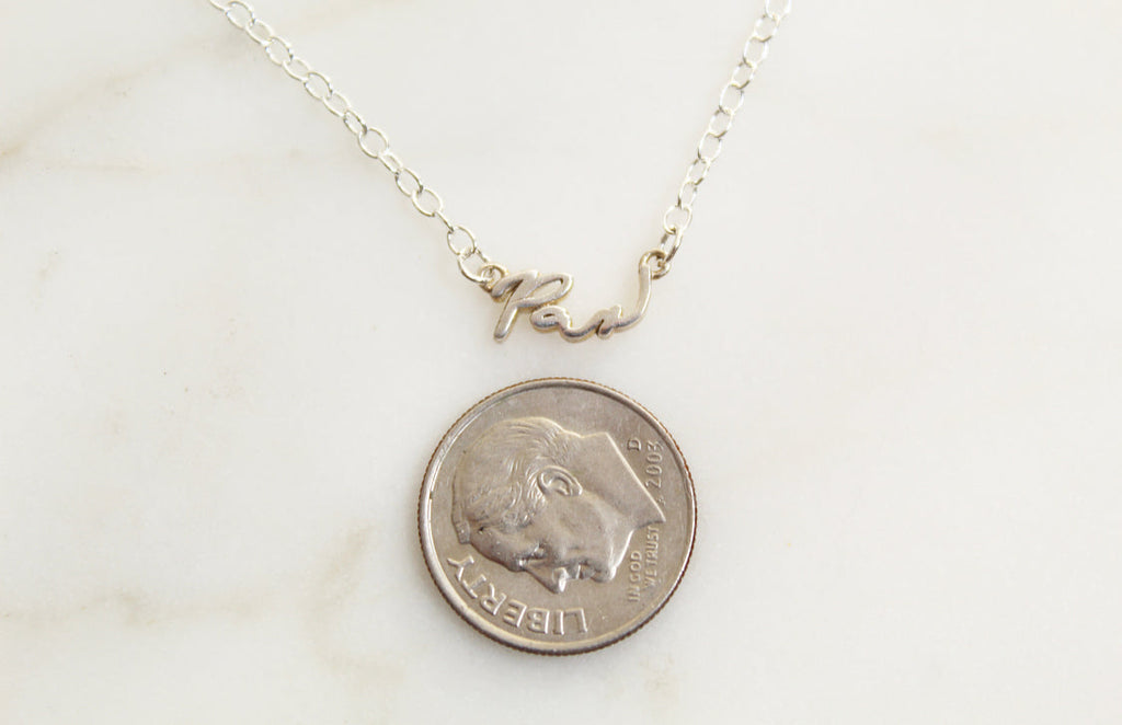 Sterling silver Pax necklace with cursive pendant shown beside a coin