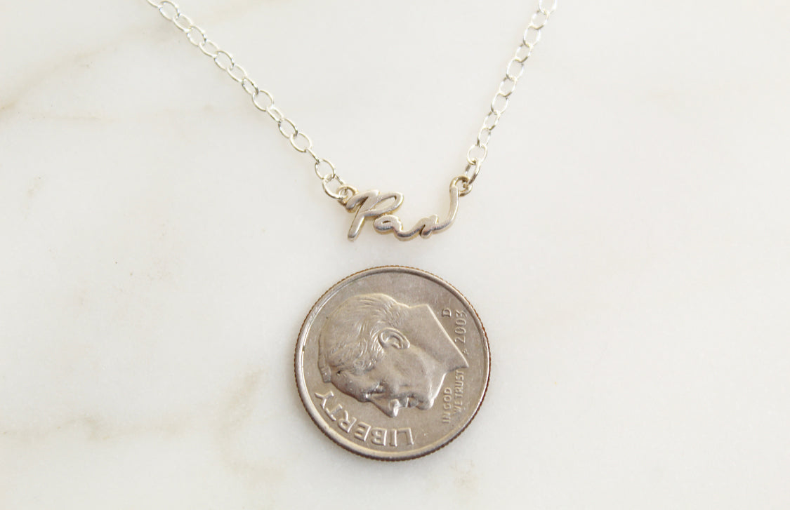 Sterling silver Pax necklace with cursive pendant shown beside a coin