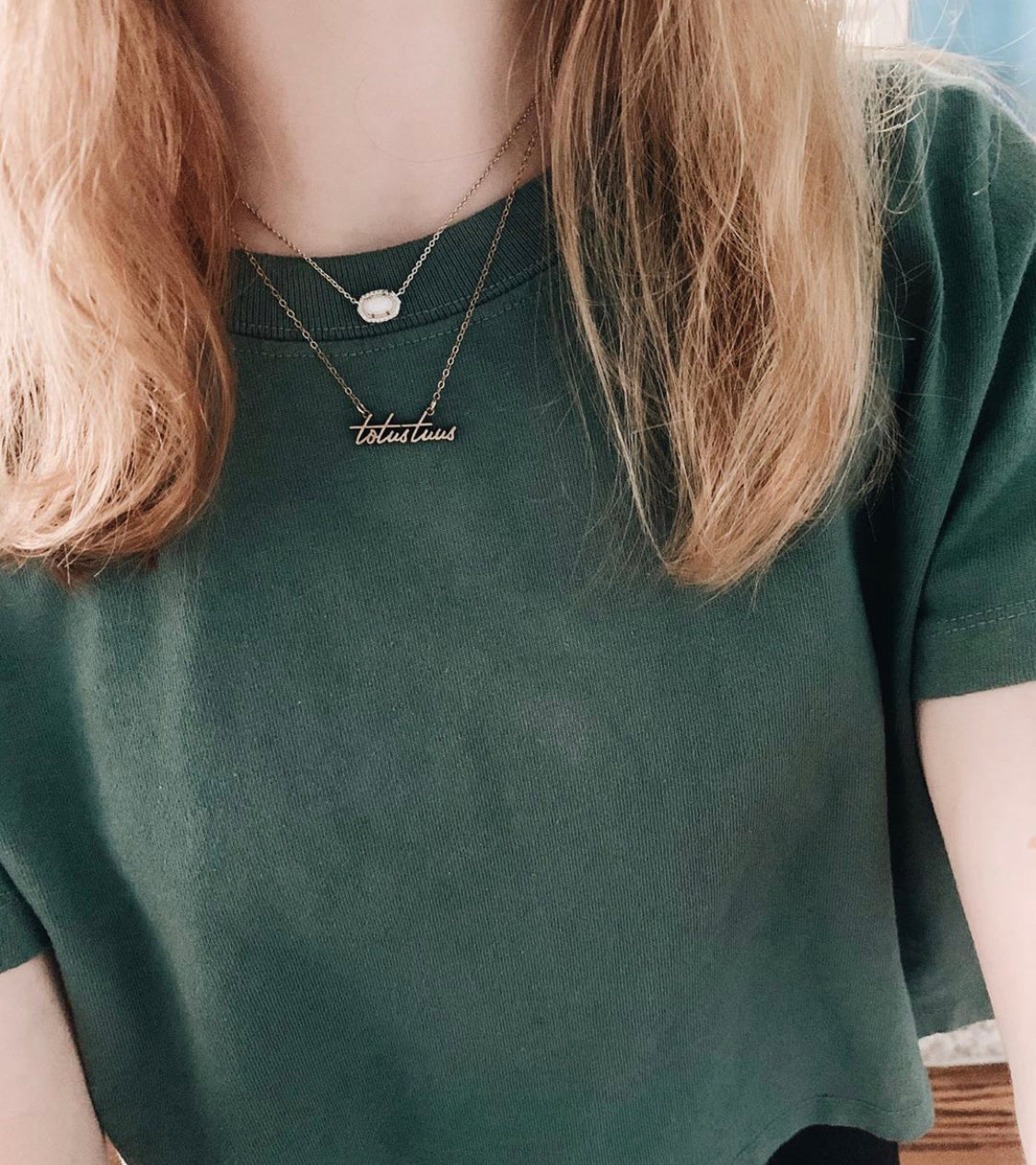 Gold-tone script pendant necklace worn at neckline on dark green shirt