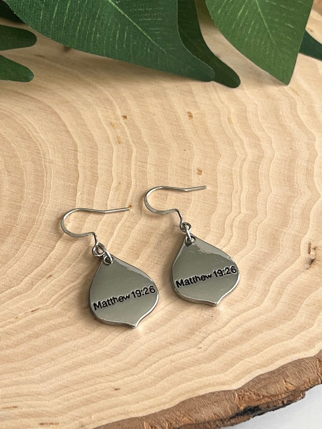 Silver teardrop charm earrings with “Matthew 19:26” text and dangling hooks.