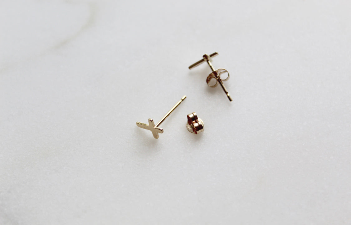 Set of cross stud earrings on a flat surface, including post and earring backs.