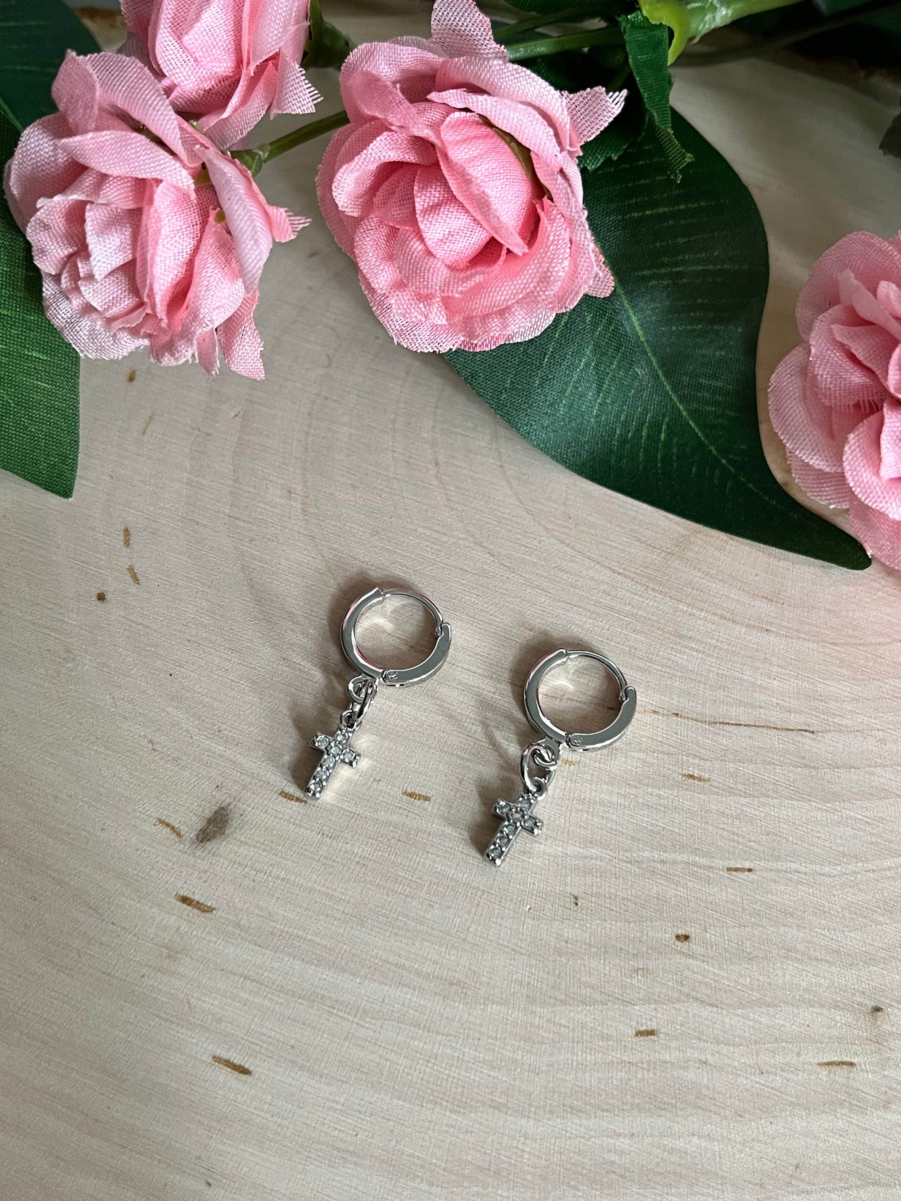 Silver huggie hoop earrings with cross charms, pair on light wood with flowers