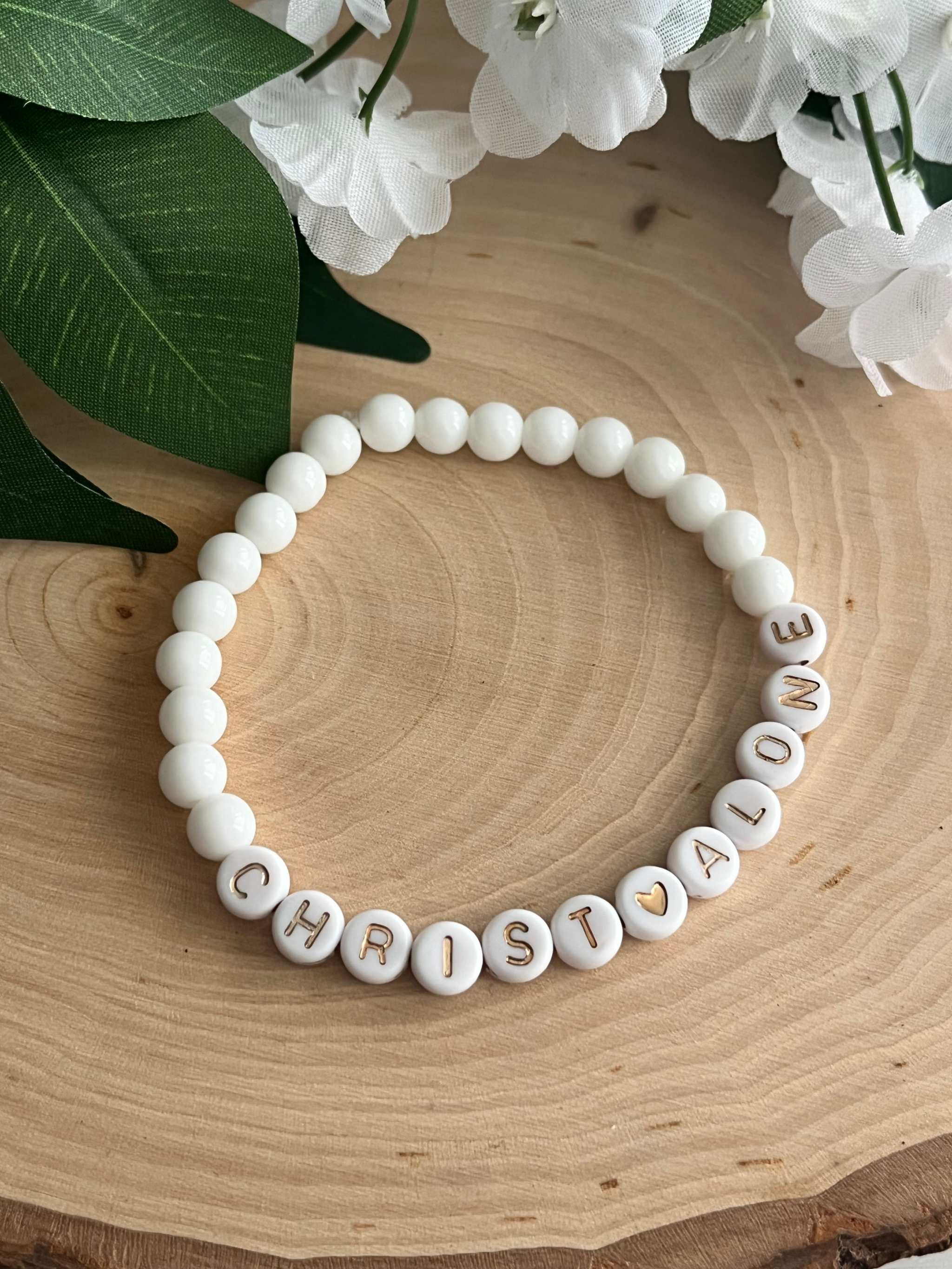 White bead bracelet with letter beads spelling "CHRIST ALONE" and small gold accents
