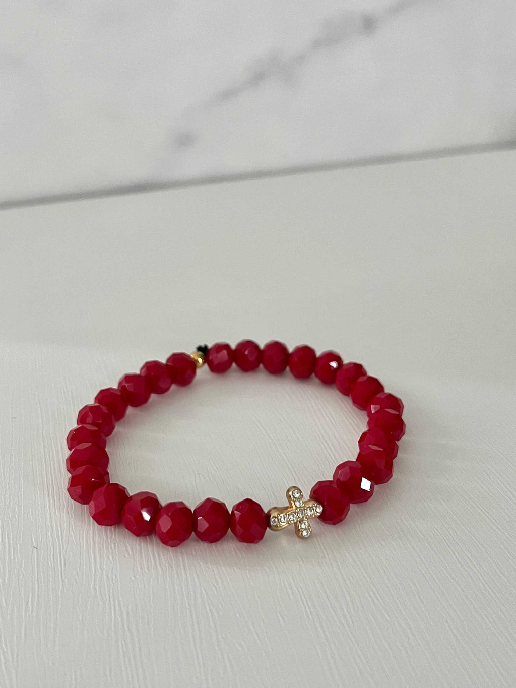 Ruby red beaded bracelet with gold cross charm, side view.