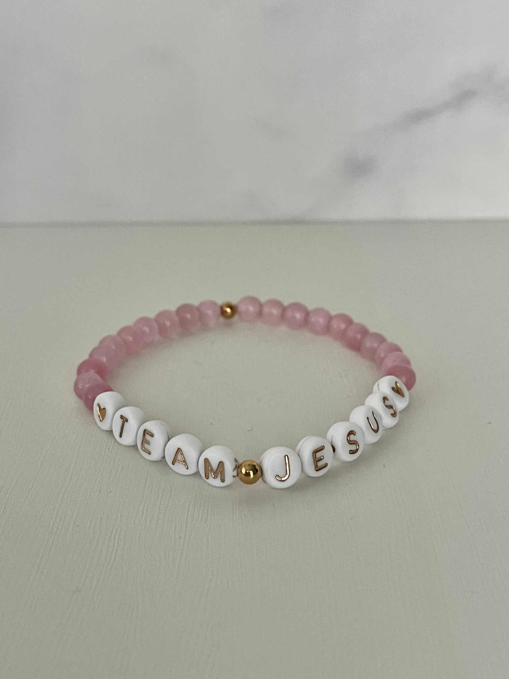 Opal-like iridescent beaded bracelet with pink beads and white letter charms spelling JESUS