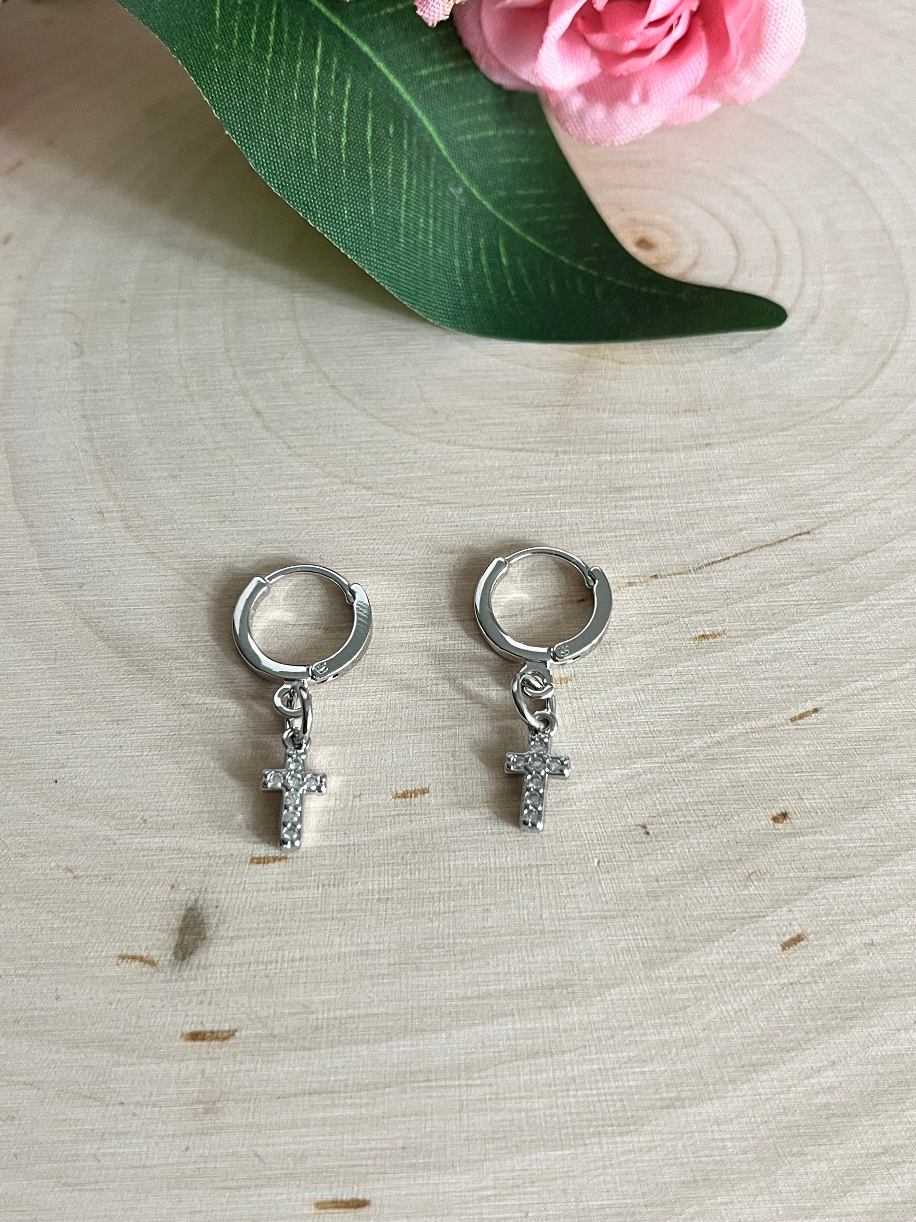 Pair of silver huggie hoop earrings with cross charms on a wood-slice surface