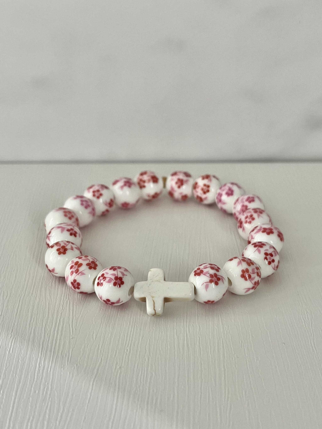 Pink floral bead cross bracelet with white cross centerpiece on a loop.