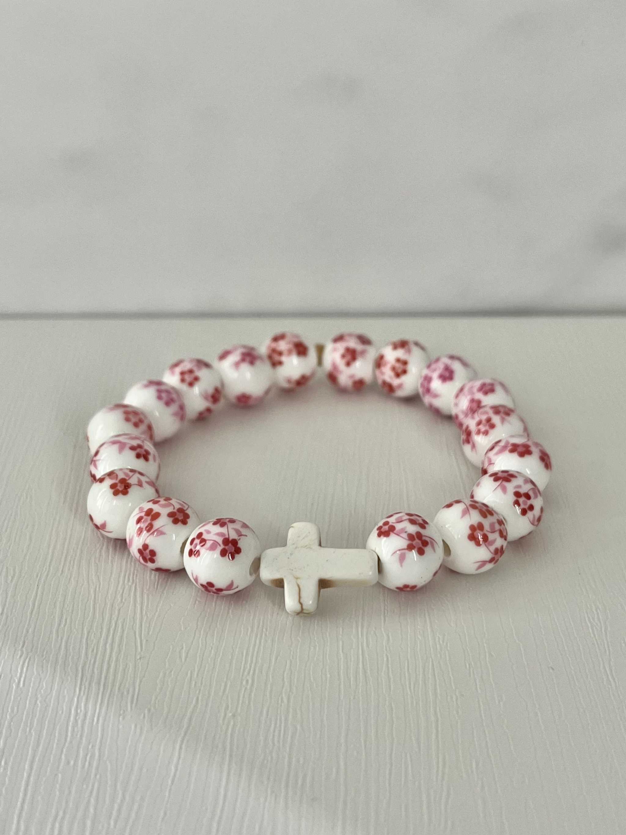 Pink floral bead cross bracelet with white cross centerpiece on a loop.
