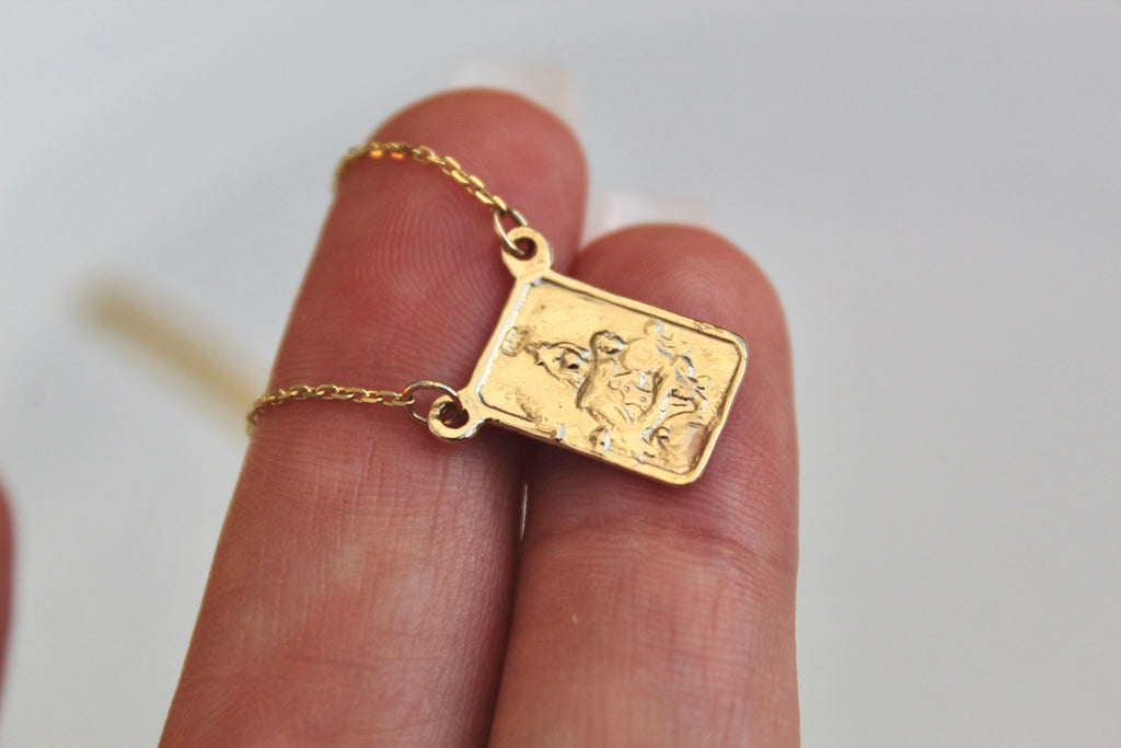 Square gold scapular pendant in palm with embossed figure, hanging on chain