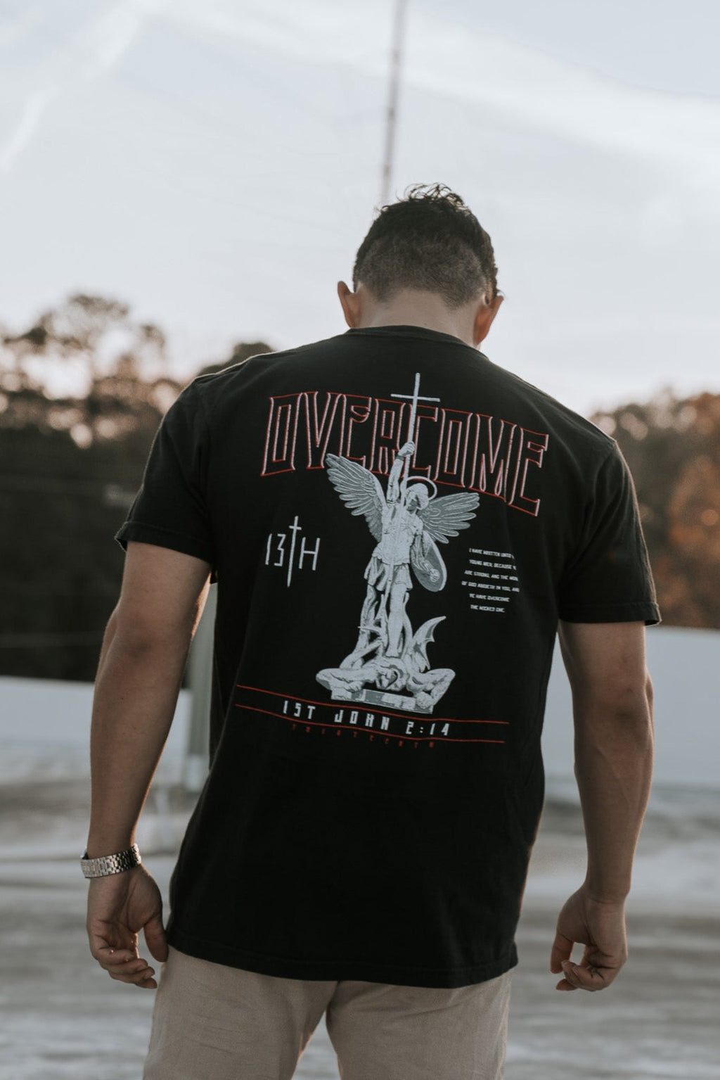 Black tee shirt with full back angel graphic and red Overcome lettering