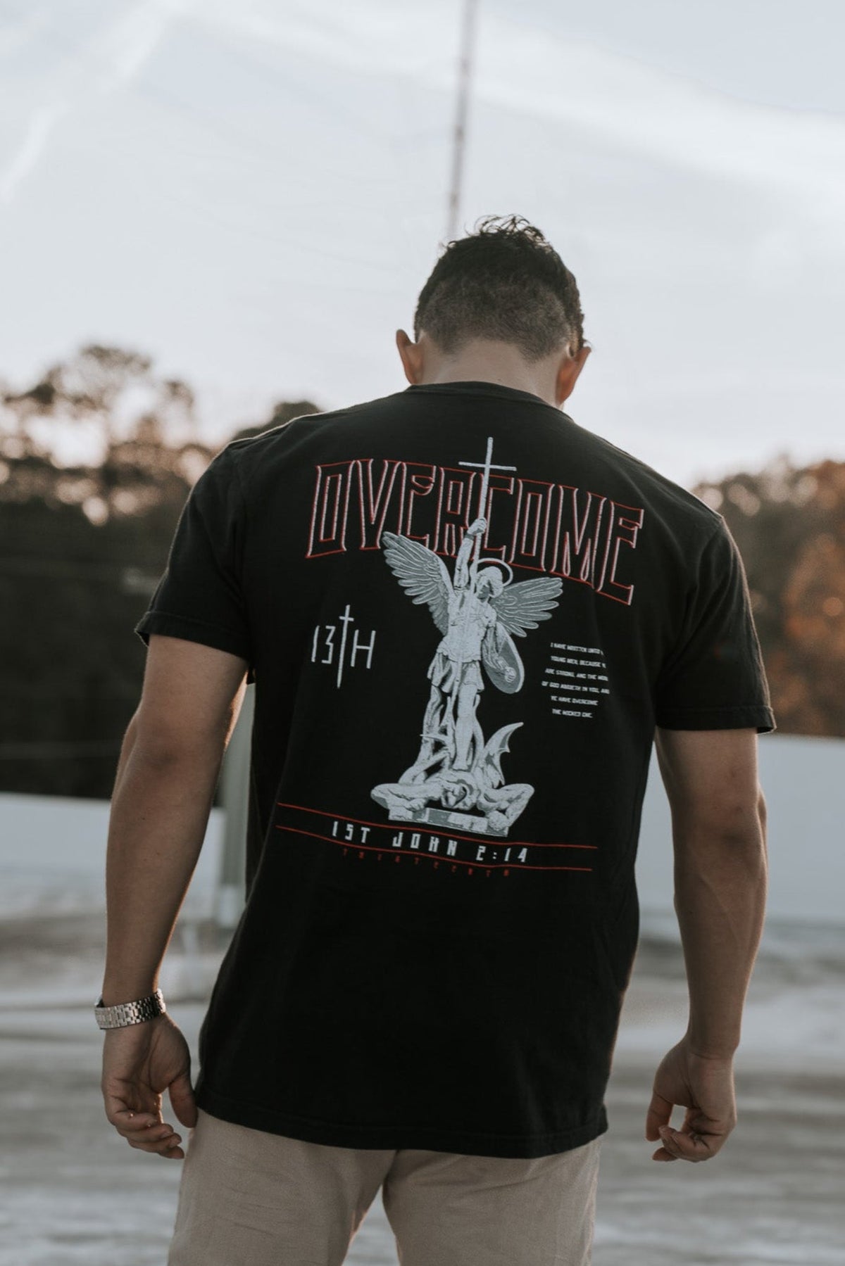 Black tee shirt with full back angel graphic and red Overcome lettering
