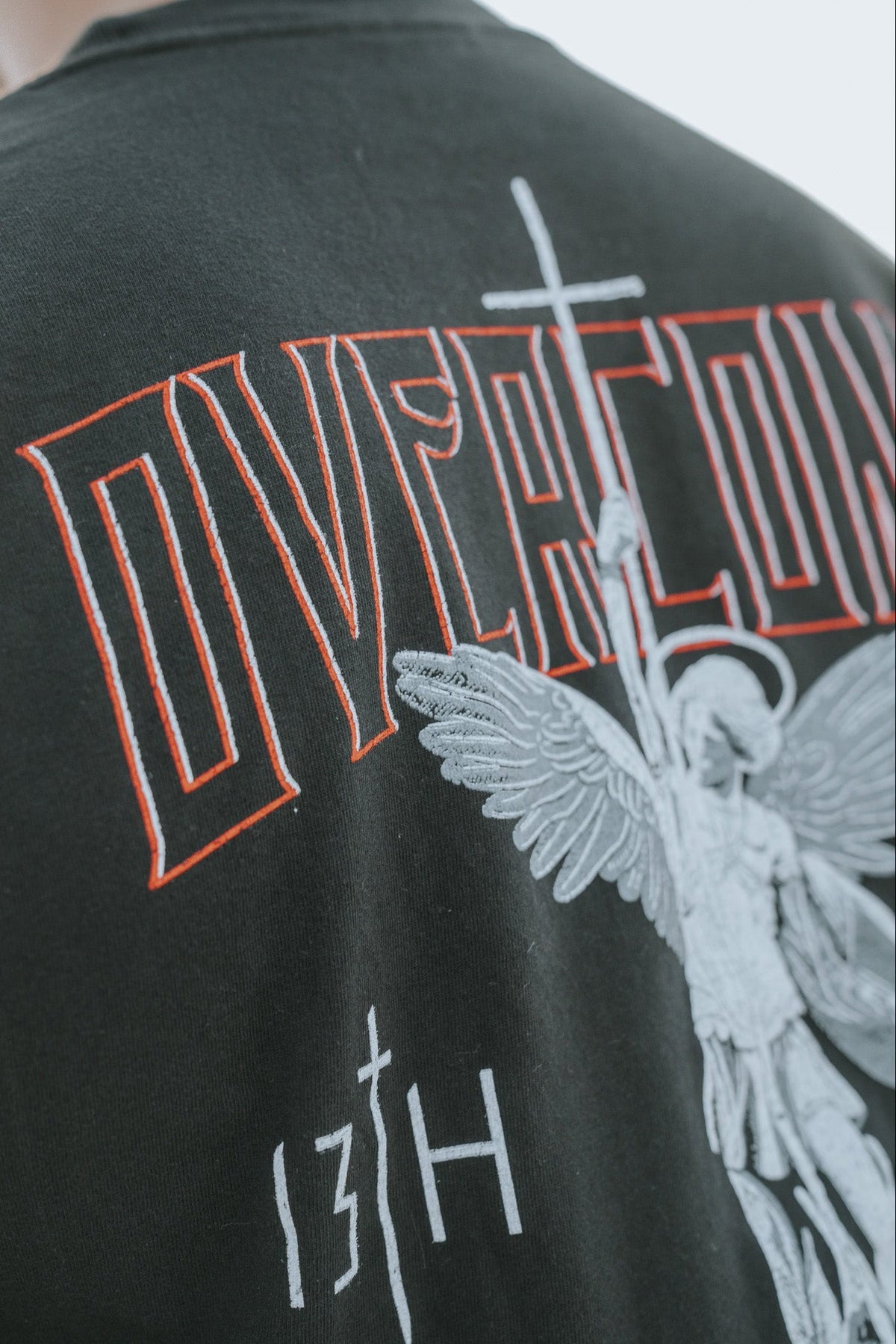 Black tee shirt close-up back shows Overcome lettering and white angel with wings