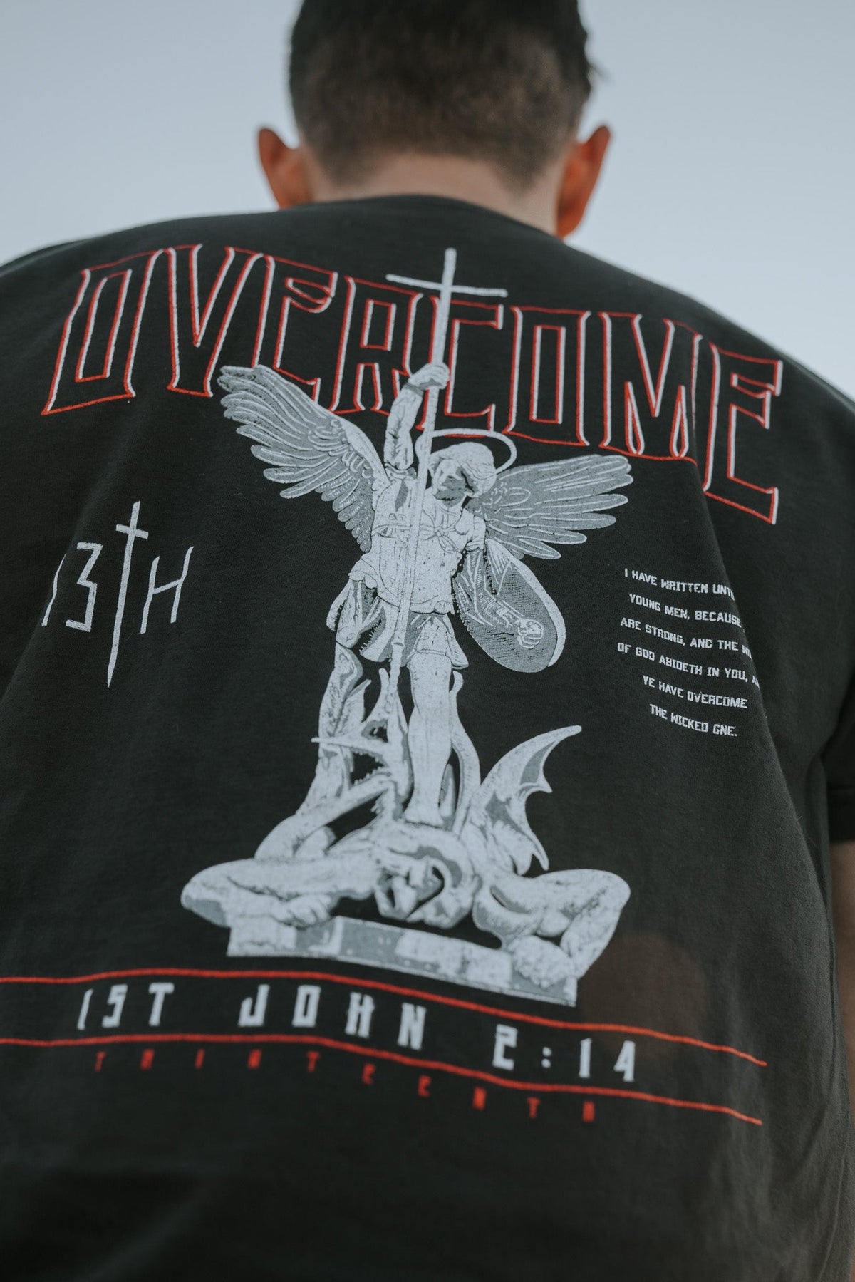 Black tee shirt close-up of back Overcome angel graphic with white wings and red outline