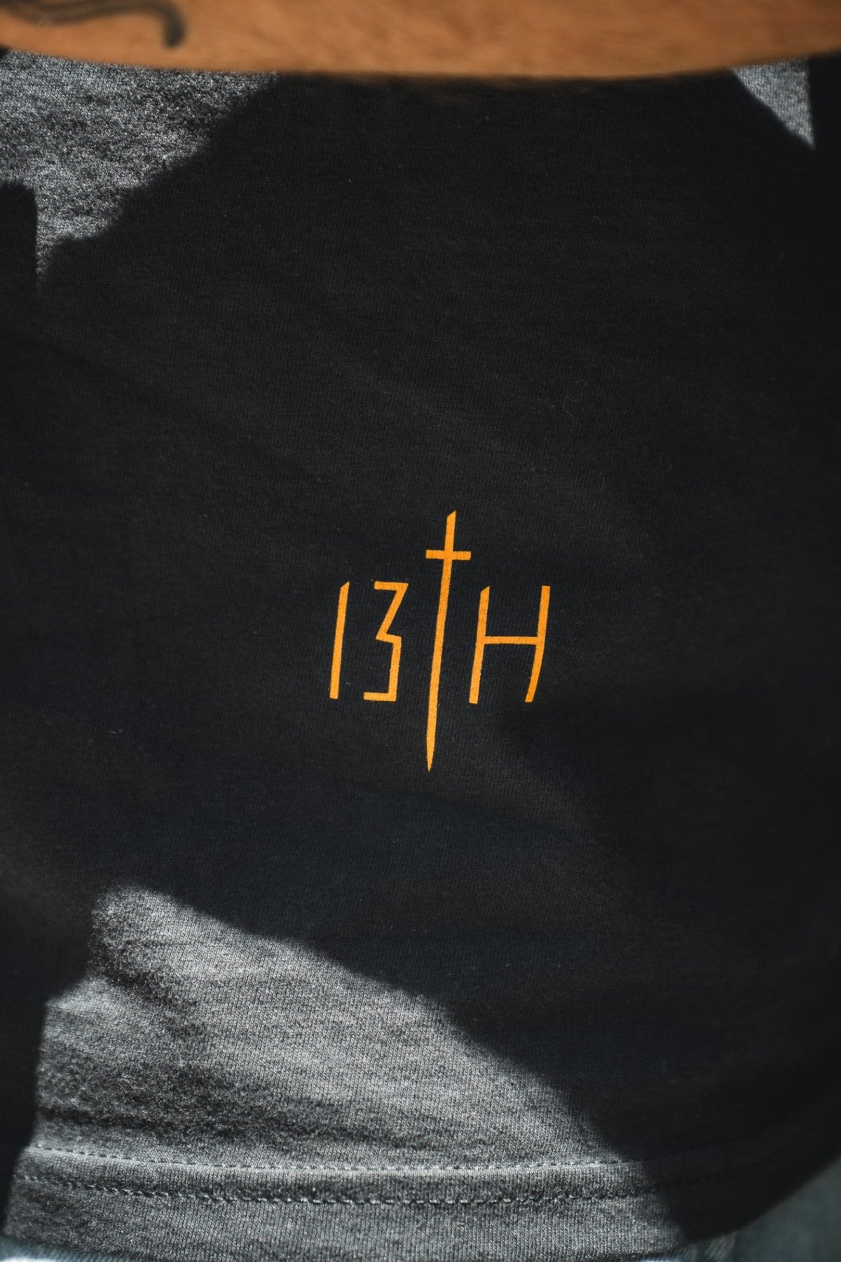 Black premium tee close-up showing orange "13th" print