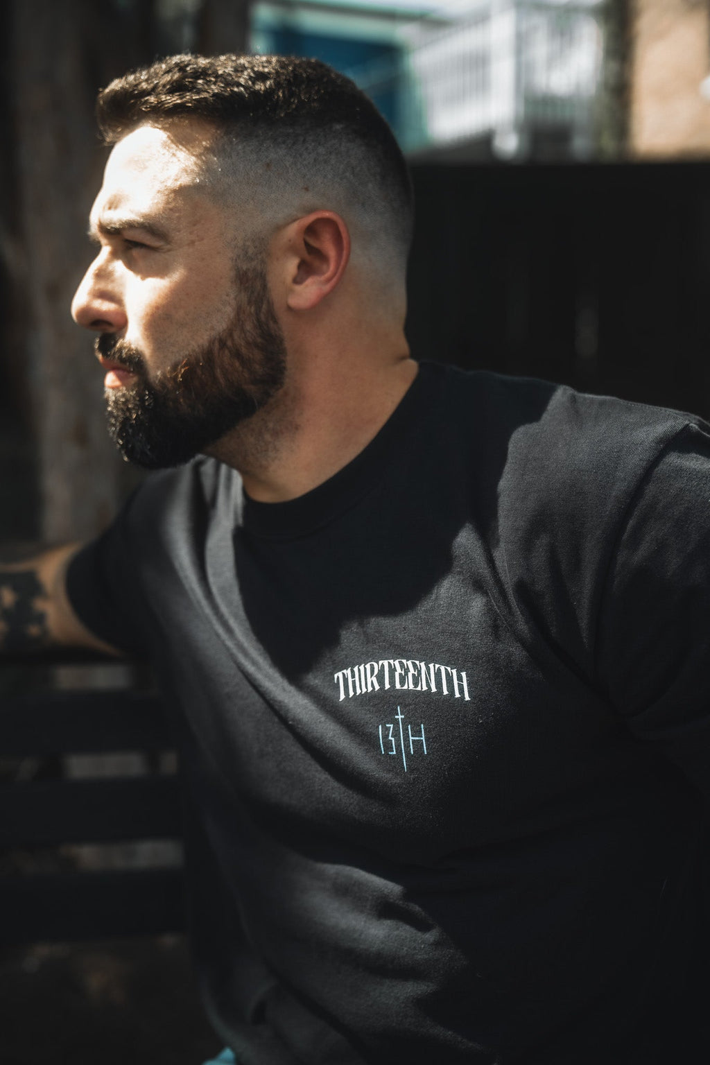 Black crewneck T-shirt with small white THIRTEENTH 13TH chest logo, side view