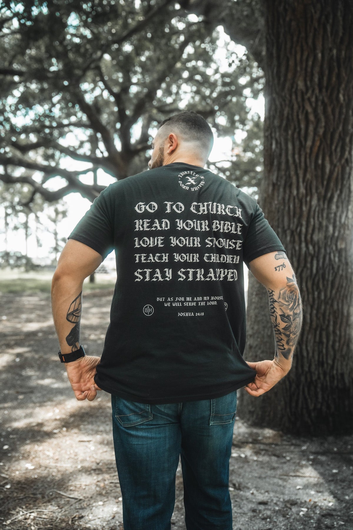 Black T-shirt back with decorative emblem above text and 'Stay Strapped' line.