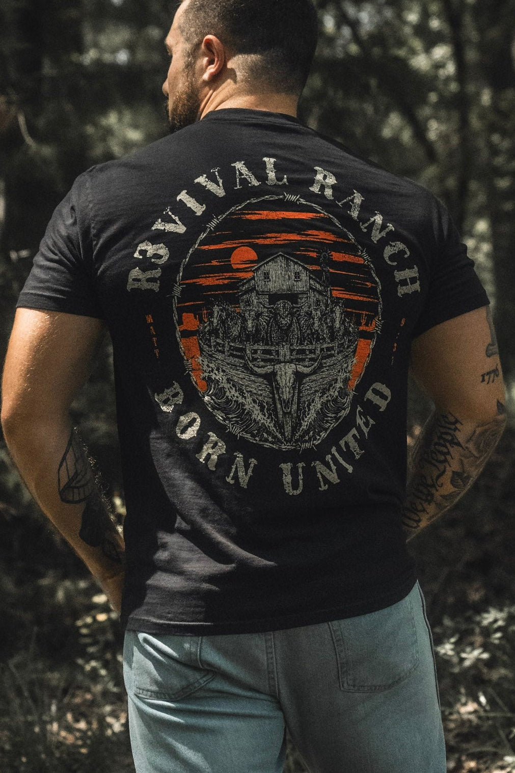 Black tee, back graphic circular emblem with orange stripes and gray farm illustration