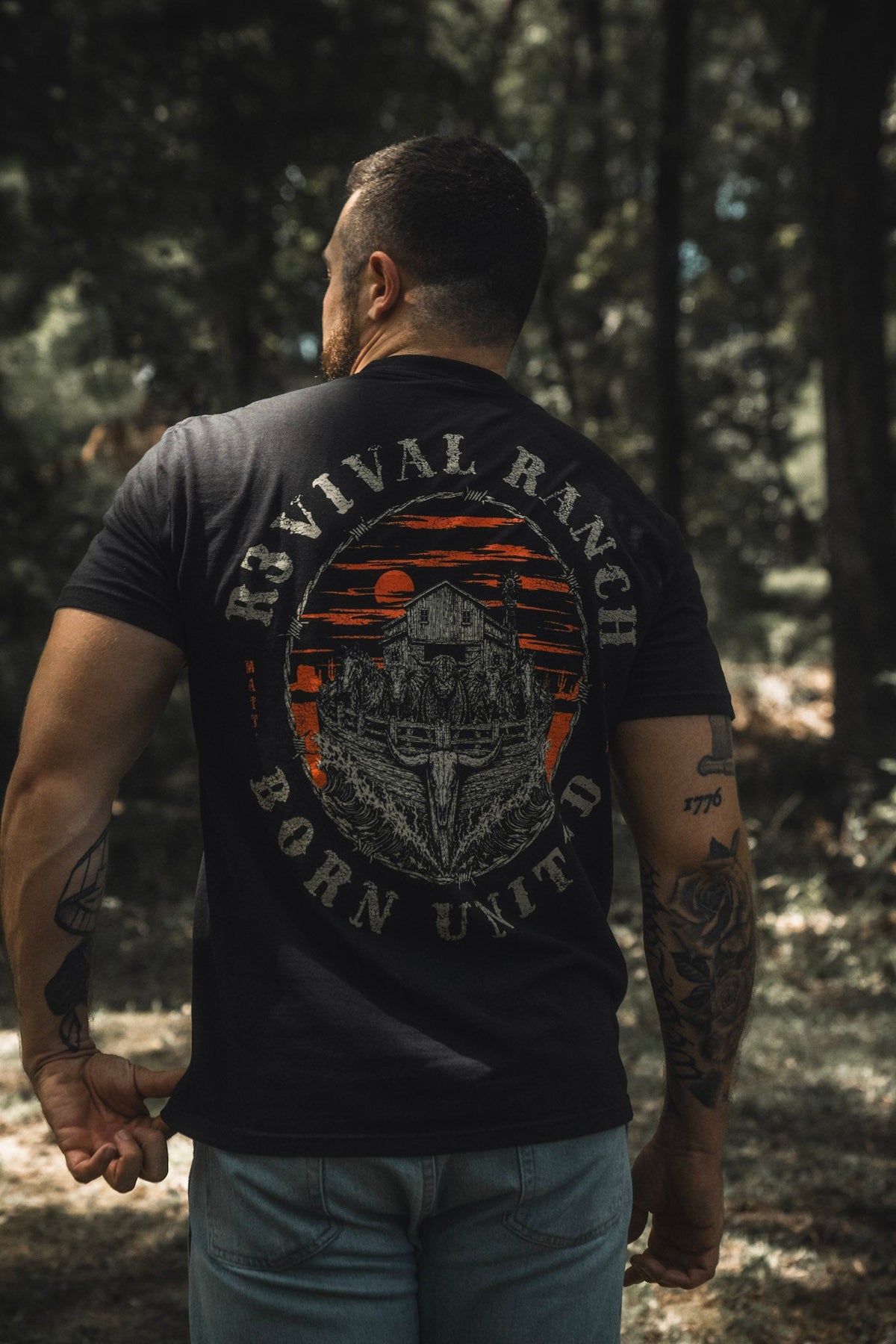 Black tee, back circular emblem graphic with orange arch and gray farm illustration