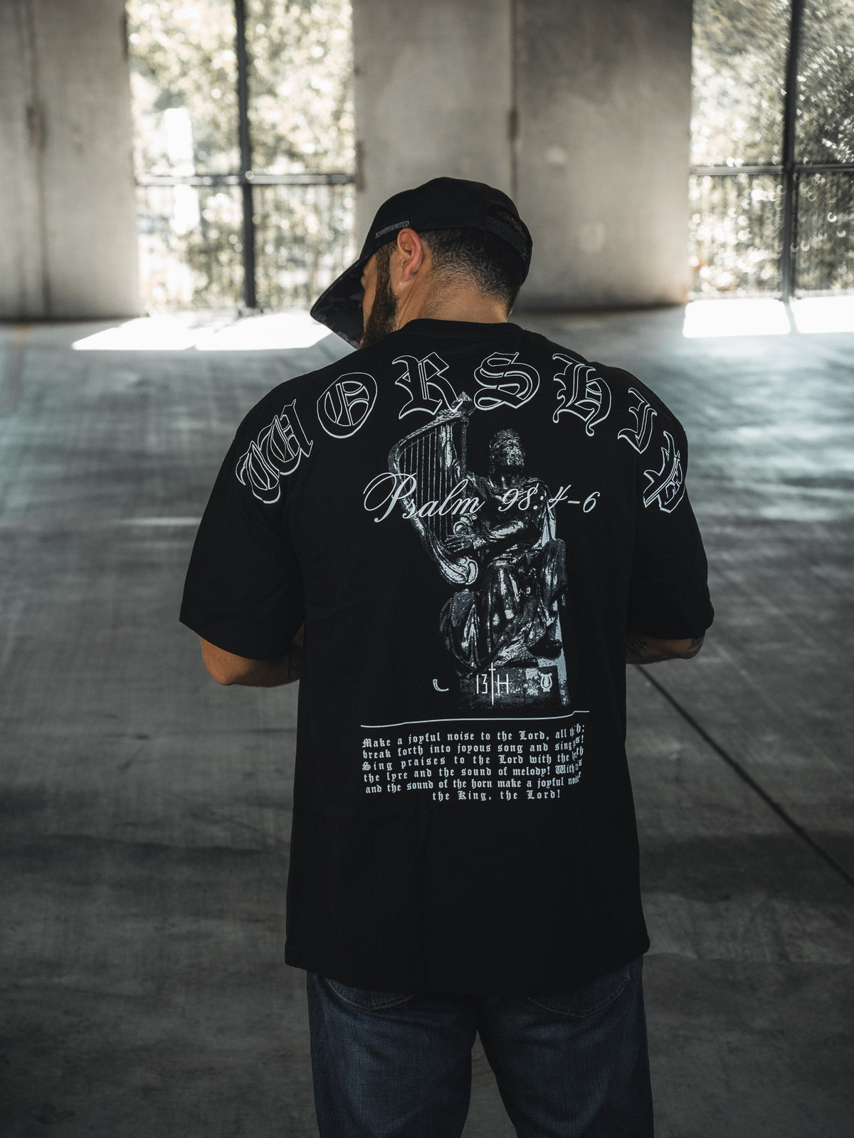 Black oversized tee with centered back graphic, portrait illustration, and script lettering.