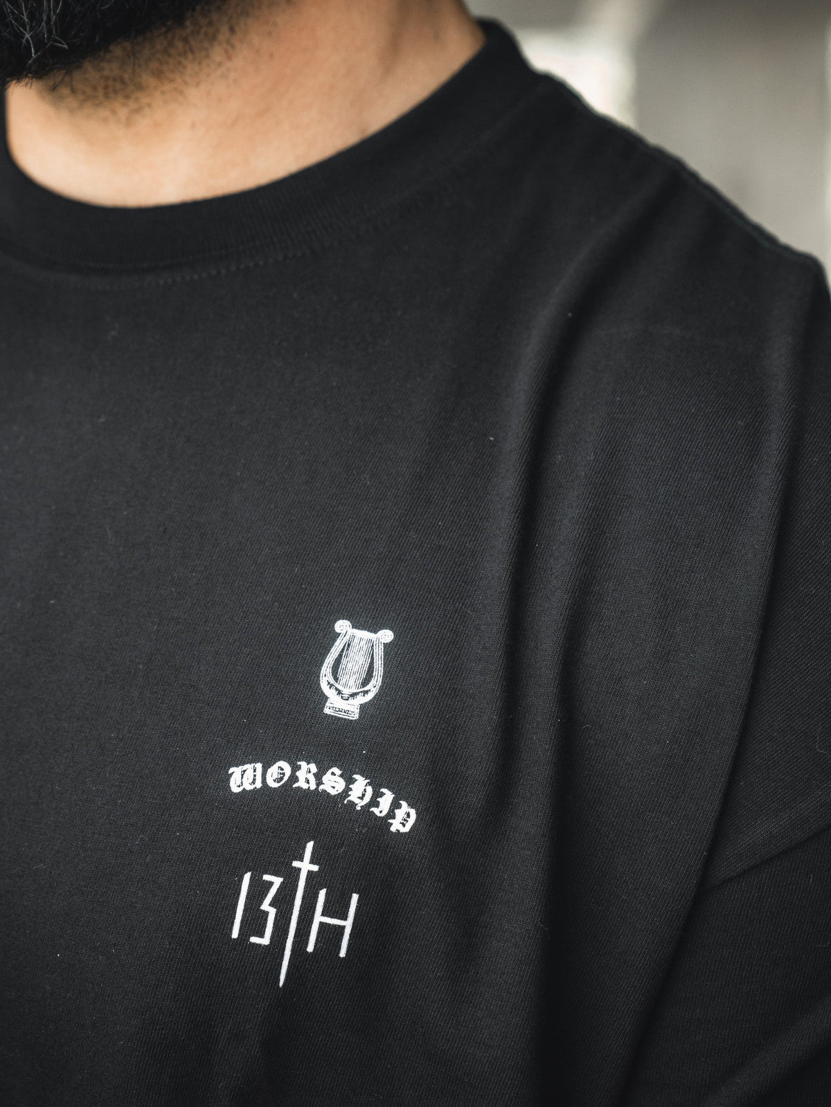 Black oversized tee chest logo with small white graphic and decorative text.