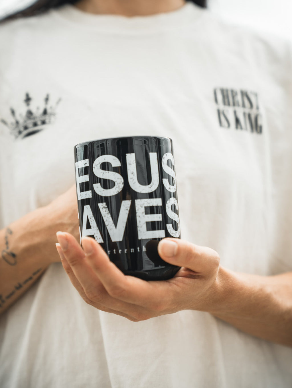 Black mug held in hands, 'JESU SAVES' with 'thirteenth' text on front