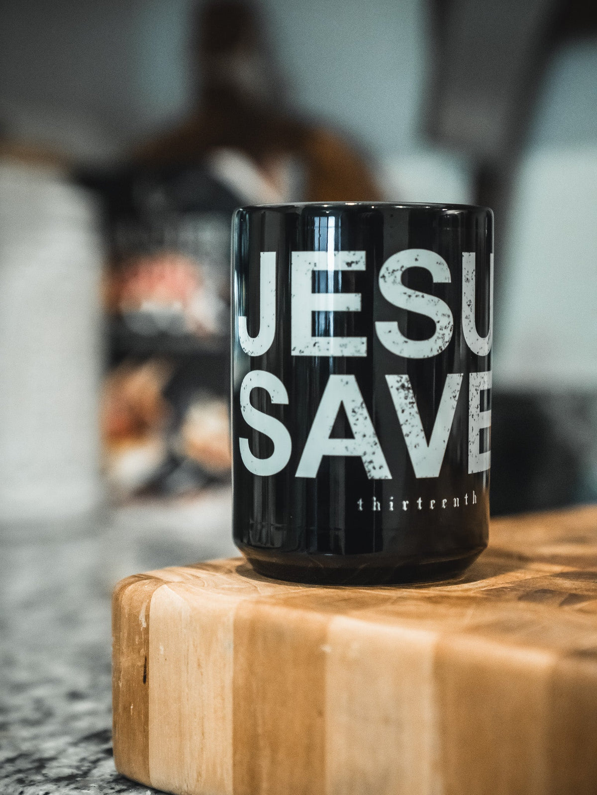 Black coffee mug on a wooden surface with 'JESU SAVE' and 'thirteenth' text