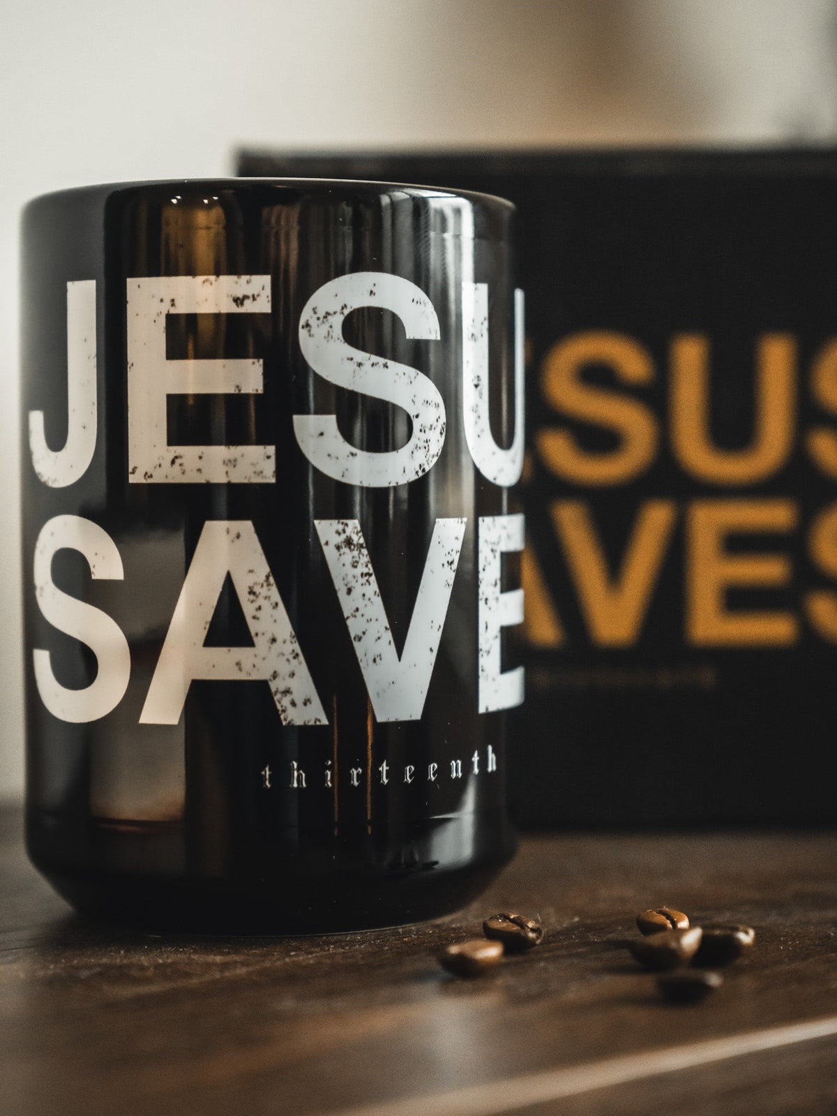 Black mug close-up with bold 'JESU SAVES' lettering and 'thirteenth' below