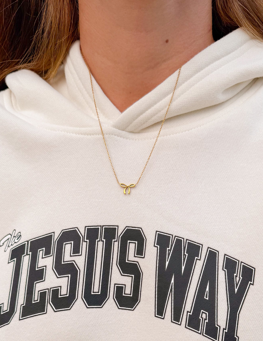 Gold bow pendant necklace on fine chain resting at the collar