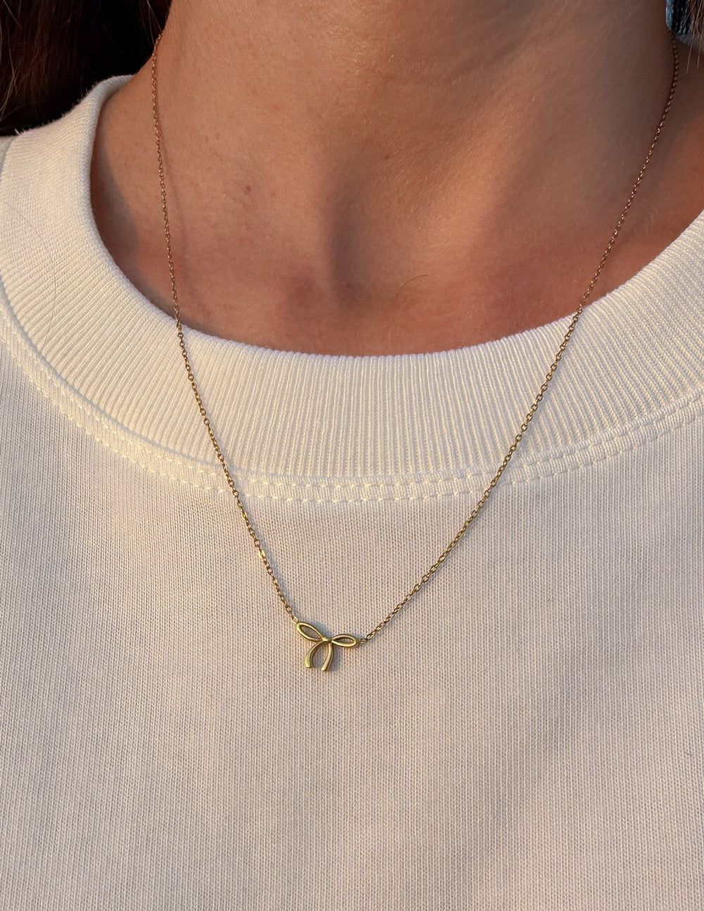 Gold bow charm necklace on fine chain with bow-shaped clasp detail