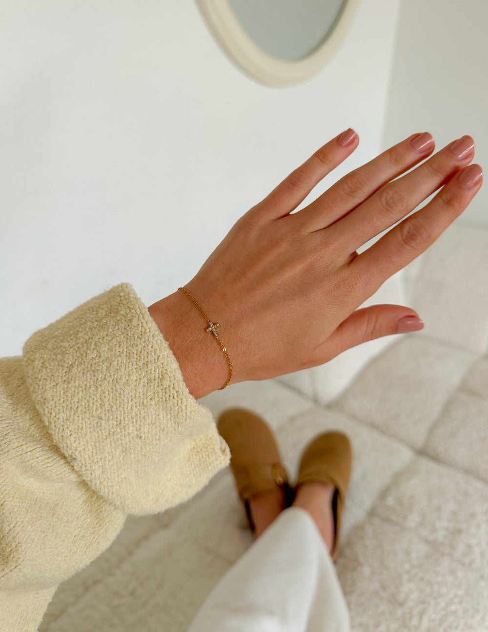 Gold cross charm bracelet on wrist with clasp detail visible.