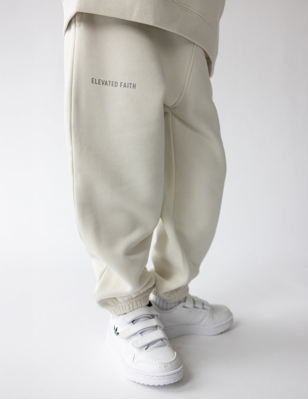 Kids cream sweatpants with 'ELEVATED FAITH' text and cuffed ankle hem