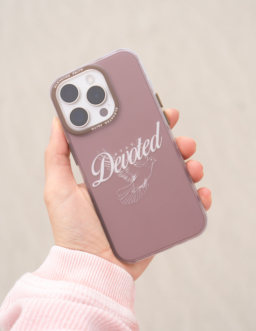 Mauve phone case with Devoted script and feather graphic, held in hand