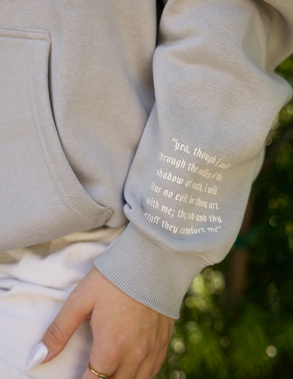 Grey hoodie sleeve with quote print and ribbed cuff; front seam visible.