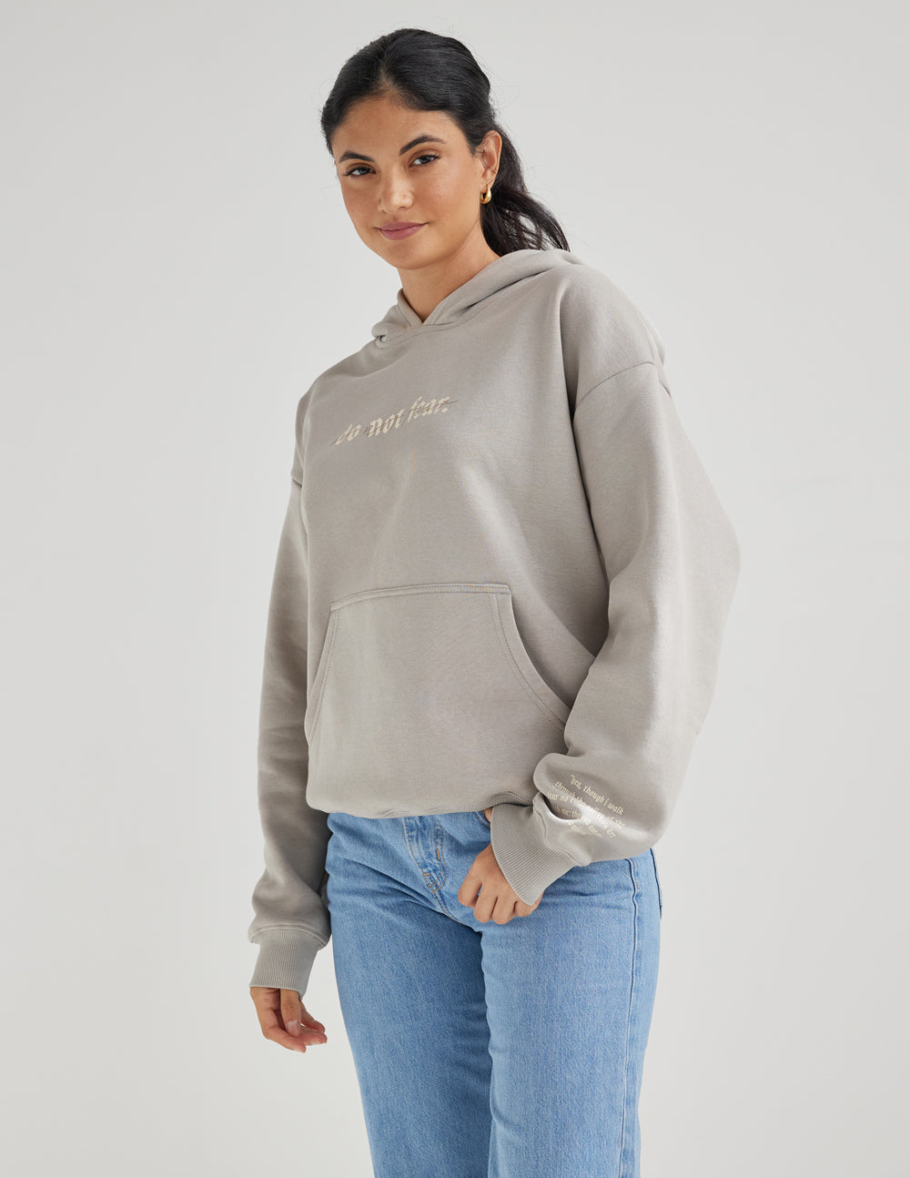 Grey unisex hoodie with hood and “do not fear.” chest print, paired with jeans.